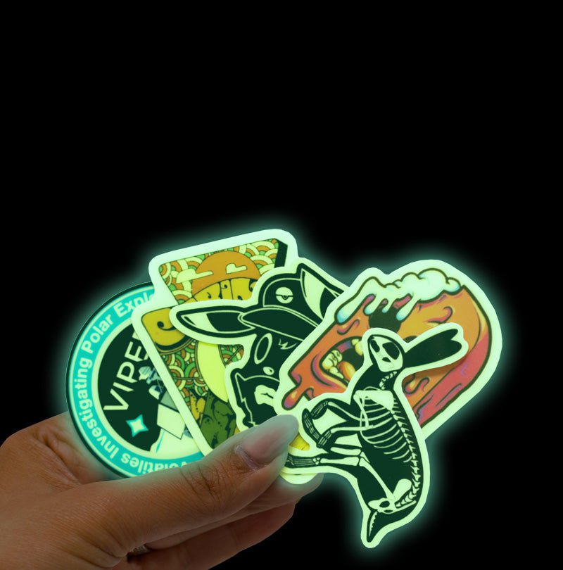 Hand holding a variety of glow in the dark stickers with illustrated graphic artwork nasa space themed viper video game cartoon character 70s poster print melting popscile and rabbit skeleton